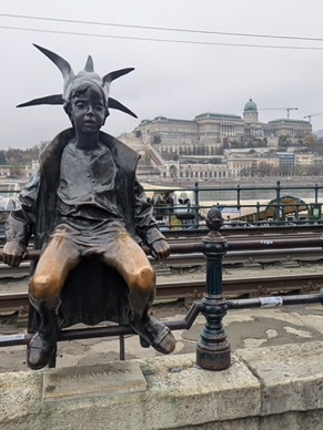 La Statue de la Petite Princesse assise sur la rambarde le long du Danube, porte une robe et une couronne pointue en papier.