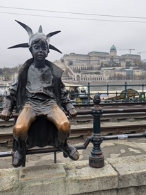 La Statue de la Petite Princesse assise sur la rambarde le long du Danube, porte une robe et une couronne pointue en papier.